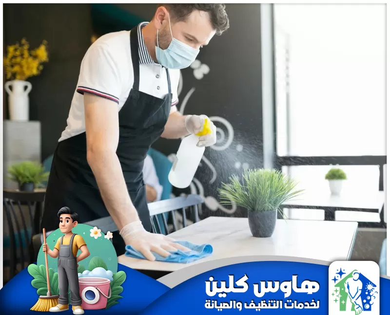 شركة تنظيف مطاعم بالرياض | 0506747660 | هاوس كلين رجل يرتدي كمامة ينظف طاولة، مُمثلاً خدمة تنظيف مطاعم في الرياض